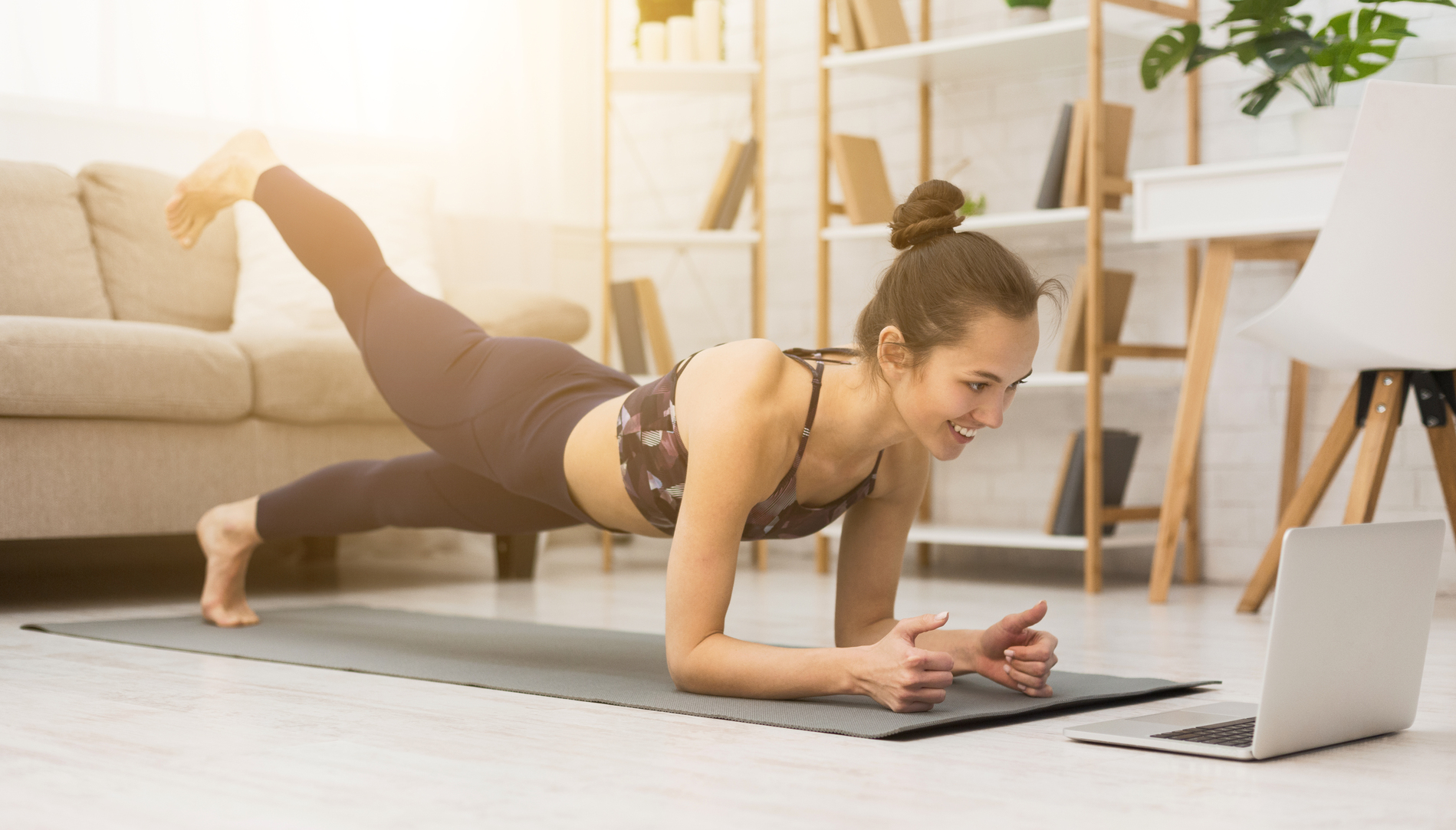 Girl training at home, doing plank and watching videos on laptop